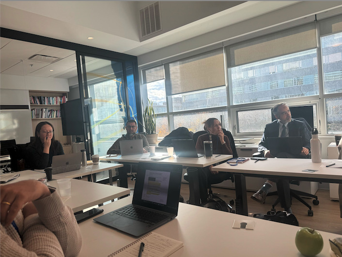 Audience members are seated in rows, listening attentively to a presentation. 